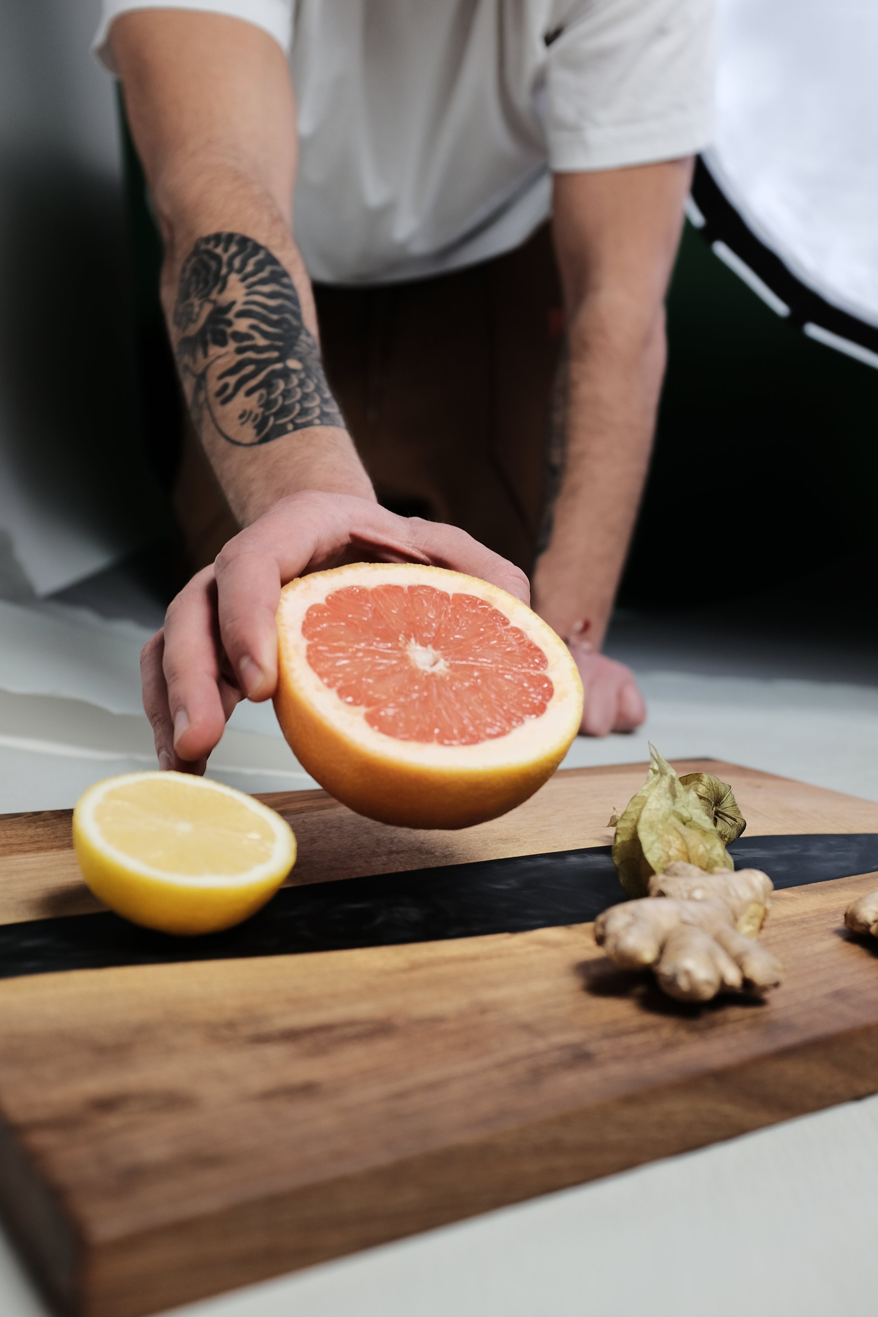 Black epoxy wooden serving board with a hand placing a grapefruit on top for decoration